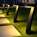 Row of matte black angular solar LED pathway lights illuminating a garden walkway with warm golden light at dusk