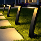 Row of matte black angular solar LED pathway lights illuminating a garden walkway with warm golden light at dusk