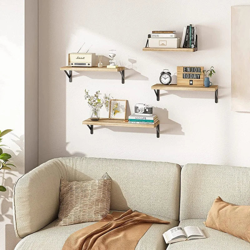 Three rustic wood floating shelves with black metal brackets styled with books, plants and decor in a modern living room