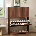 Walnut shoe cabinet with upper flip-door closed and lower compartment open showing two rows of sneakers, styled in a warm entryway with bench and plant