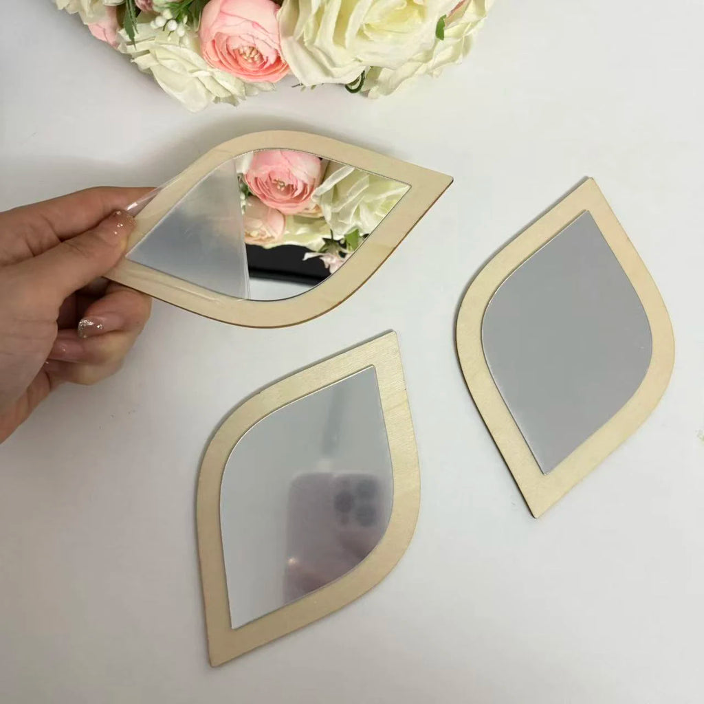 Hand holding a leaf-shaped wood frame mirror showing three sizes arranged on a white surface