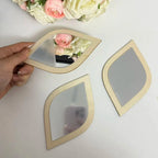 Hand holding a leaf-shaped wood frame mirror showing three sizes arranged on a white surface