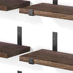 Close-up detail of dark walnut wood grain texture and matte black metal bracket hardware on floating wall shelves